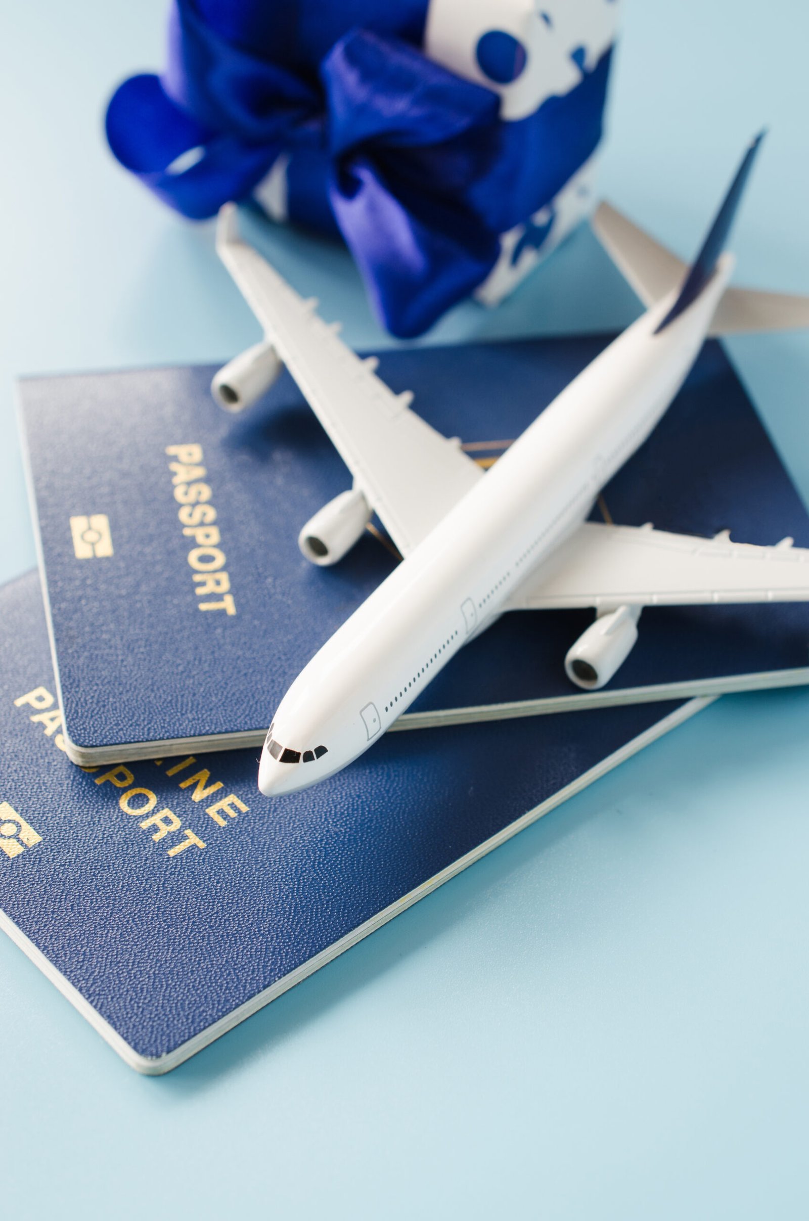 Traveling as gift. White blank model of passenger plane, passports and gift box on blue background. Christmas travel planning. Top view or flat lay. Copy Space.